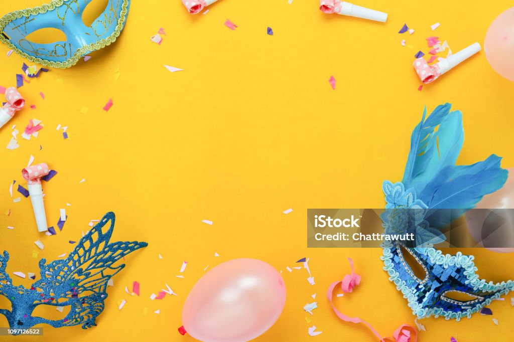 Table top view aerial image of beautiful colorful carnival festival background.Flat lay accessory object the mask & decor confetti and balloon on modern yellow paper at home office desk studio. Carnival - Celebration Event Stock Photo