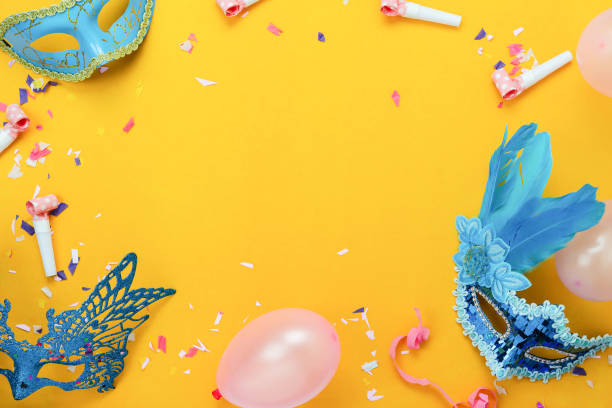 Table top view aerial image of beautiful colorful carnival festival background.Flat lay accessory object the mask & decor confetti and balloon on modern yellow paper at home office desk studio. stock photo