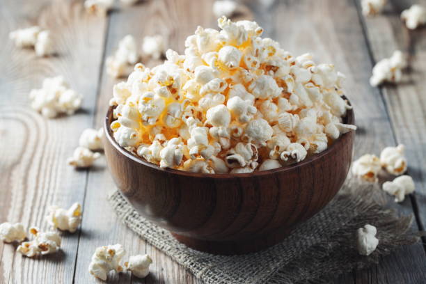 un cuenco de madera de palomitas de maíz saladas en la vieja mesa de madera. fondo oscuro. enfoque selectivo - popcorn fotografías e imágenes de stock