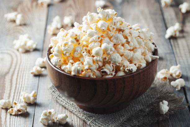 A wooden bowl of salted popcorn at the old wooden table. Dark background. selective focus A wooden bowl of salted popcorn at the old wooden table. Dark background. selective focus. crucifers stock pictures, royalty-free photos & images