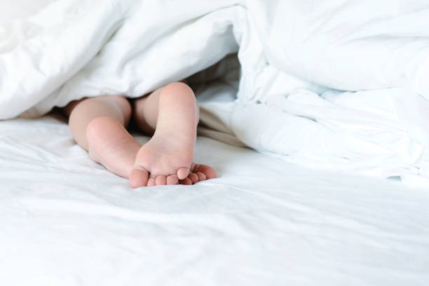 istock From under a white blanket, stick bare children's feet. Copy space. Bright photo in bed with space for text. 1097133478