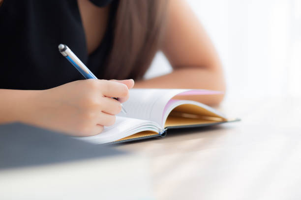 istock Closeup hand asian woman sitting study and learning writing notebook and diary on table in living room at home, girl homework, business writer woman working on table, education concept. 1097145086