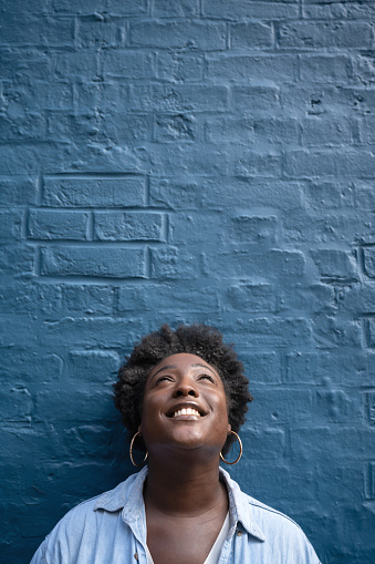 Thoughtful black woman looking happy leaning against a brick wall and smiling - lifestyle concepts