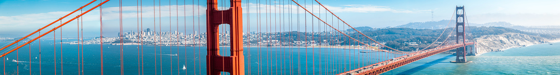 Panoramic view of famous Golden Gate Bridge with the skyline of San Francisco in the background on a beautiful sunny day with blue sky and clouds in summer, California, USA