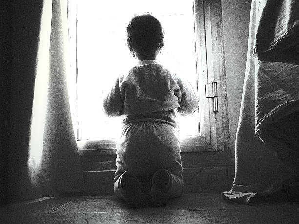 Young Girl Kneeling While Looking Out Window, Black and White stock photo