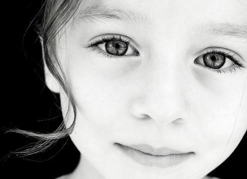 Portrait of a cute female child looking straight at camera and smiling. Monochrome photography concept.