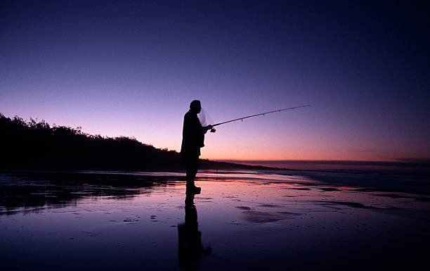 Silhouette of Man Fishing at Sunset stock photo
