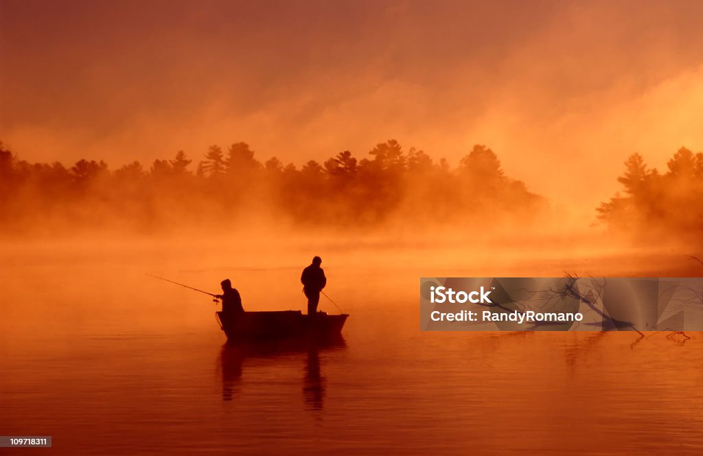 Silhouette of two fishermen on boat on a misty river Two fishermen wait for a fish to bite on a beautiful misty morning Color Image Stock Photo