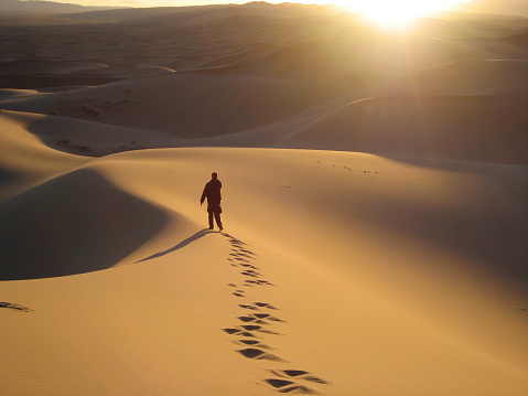 From above of dry sandy terrain of dunes in White Sands National Park with anonymous male traveler walking through desert