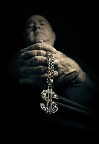 low light- low angled photo of a priest with a bling-bling chain and dollar sign instead of a rosary