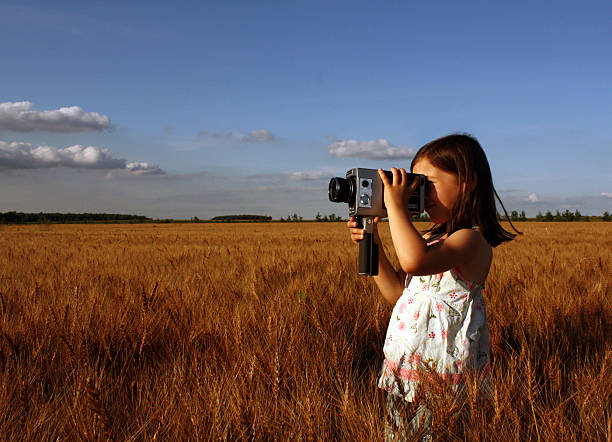 petite fille debout dans le champ et filmer avec appareil photo vintage - raid 5 photos et images de collection