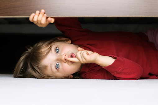 Happy mom and adorable little child girl having fun in play tent, resting on heating floor in handmade toy fort from chairs and blanket, talking, chatting, laughing