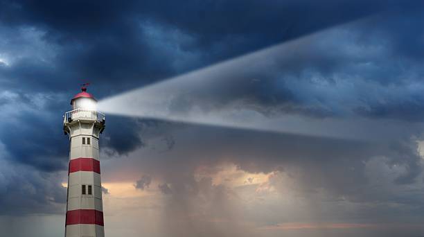 faro parzialmente illuminato da luce naturale, il brutto tempo in background - luce del faro foto e immagini stock