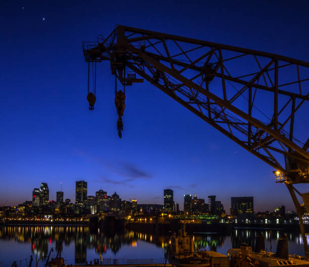 'Montreal skyline and Saint Laurent river at st night . there is a loading crane from the port seen in the foreground.