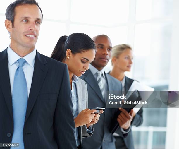 Photo libre de droit de Femme Daffaires À Laide De Téléphone Portable Et Debout Avec Ses Collègues banque d'images et plus d'images libres de droit de 20-24 ans