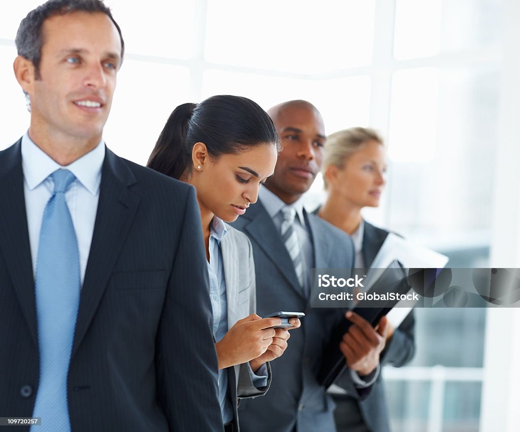 Donna d'affari con cellulare e in piedi con i suoi colleghi - Foto stock royalty-free di 20-24 anni