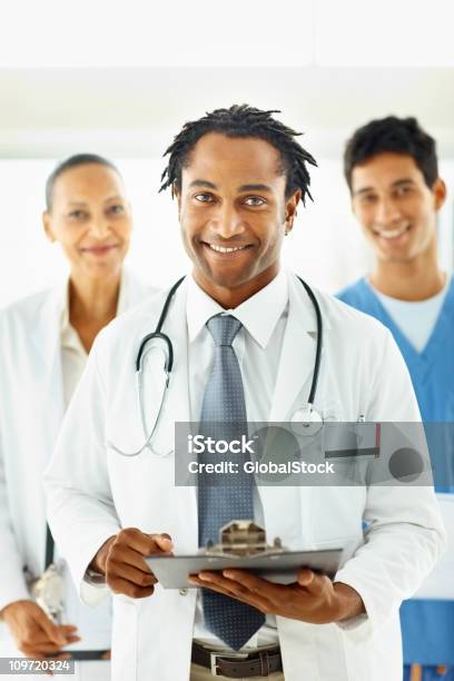African American Médico Con Colegas En La Parte Posterior Foto de stock y más banco de imágenes de Doctor