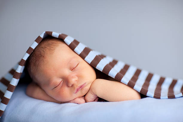 Newborn Baby Boy Sleeping Peacefully Under Striped Blanket