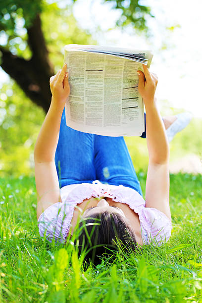 istock Young woman reading newspaper lying on the grass. 109720621