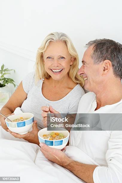 Sonriente Pareja De Jubilados Con Su Desayuno En La Cama Foto de stock y más banco de imágenes de 55-59 años