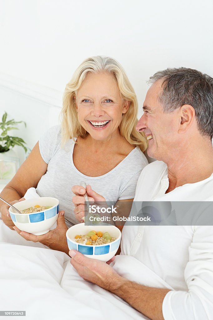 Souriant couple de retraités ayant leur petit déjeuner au lit - Photo de 55-59 ans libre de droits