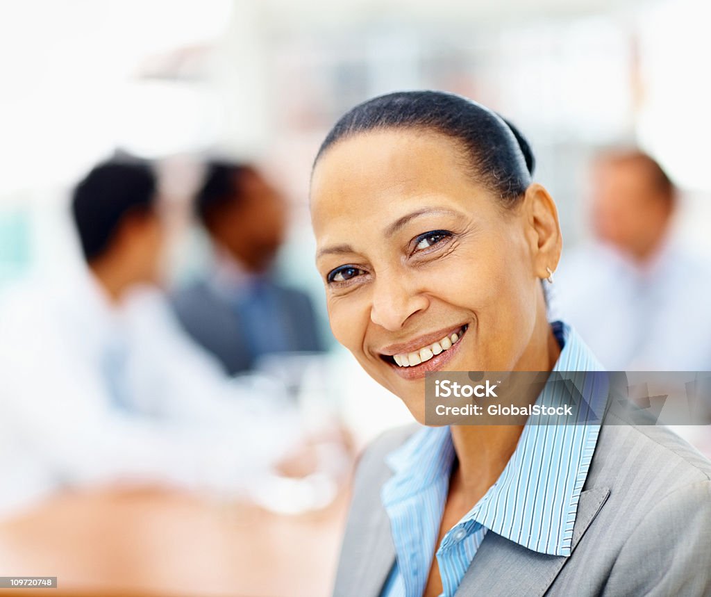 Matura donna d'affari sorridente con coleagues sul retro - Foto stock royalty-free di 20-24 anni