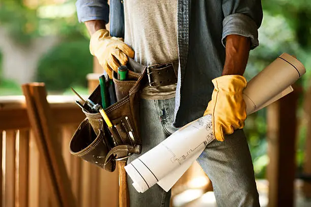 Partial view of a construction worker standing with a tool belt blueprints. Horizontal shot.