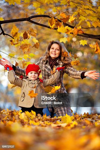 Mãe E Filha Atirando Seco Folhas No Outono Park - Fotografias de stock e mais imagens de 6-7 Anos - 6-7 Anos, Adulto, Alegria