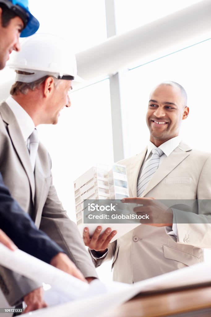 Uomo d'affari sorridente, mostrando di architettura modello per i suoi colleghi - Foto stock royalty-free di Adulto