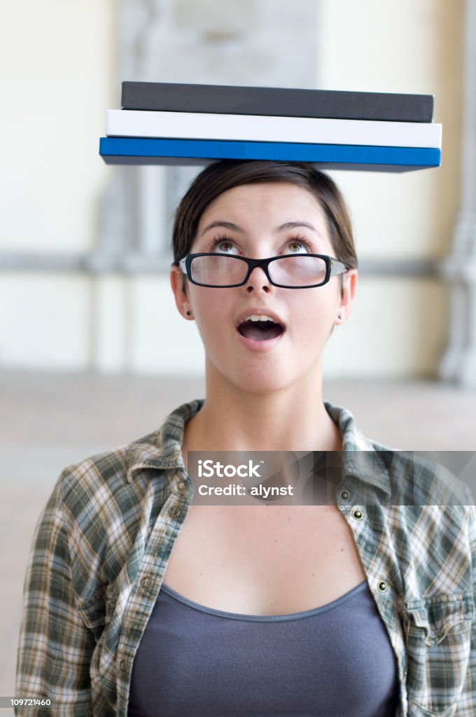 Estudiante mujer mirando sorprendido contabilización de los libros de texto sobre la cabeza - Foto de stock de 18-19 años libre de derechos