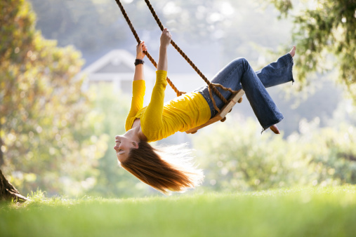 Attractive young woman hangs her head back while seated on a swing made of wood and rope. Horizontal shot.