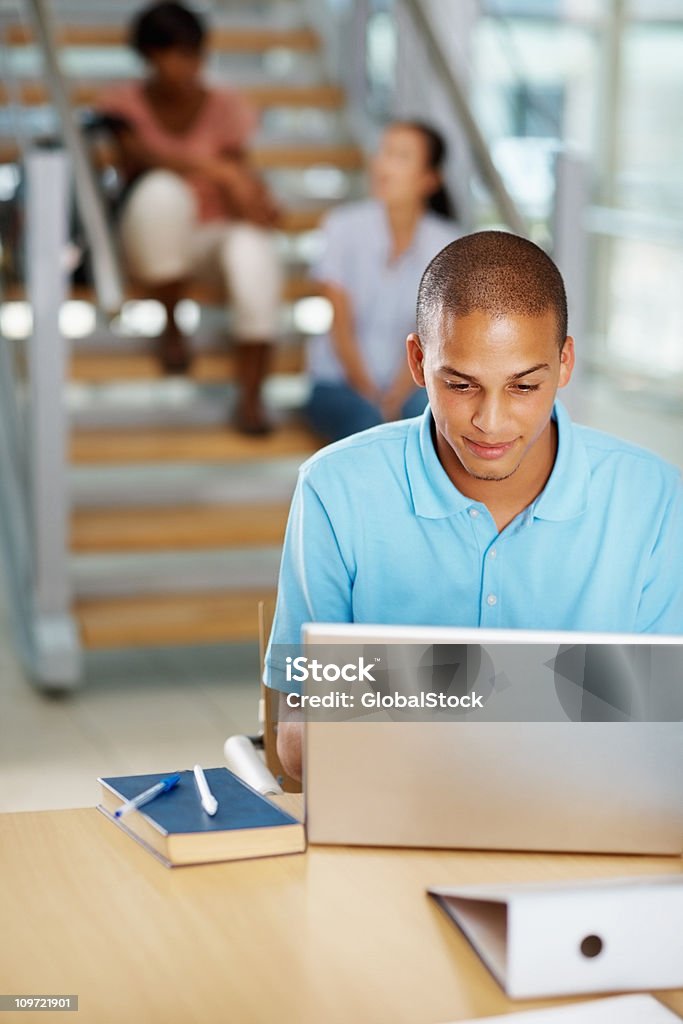 Maschio studente utilizzando il computer portatile con gli amici sul retro - Foto stock royalty-free di 20-24 anni