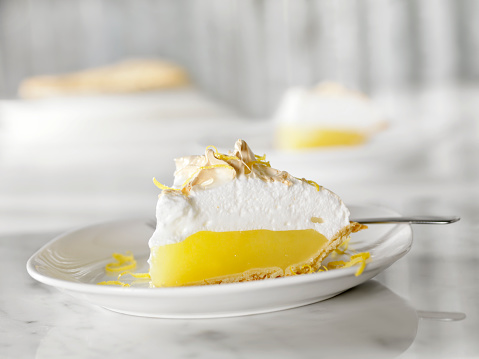 Lime cheesecake pie slice with copy space. Close-up of a delicious sweet citrus dessert. Serving of a baked cheesecake with digestive biscuit base served on a white plate with fork and green lime slices