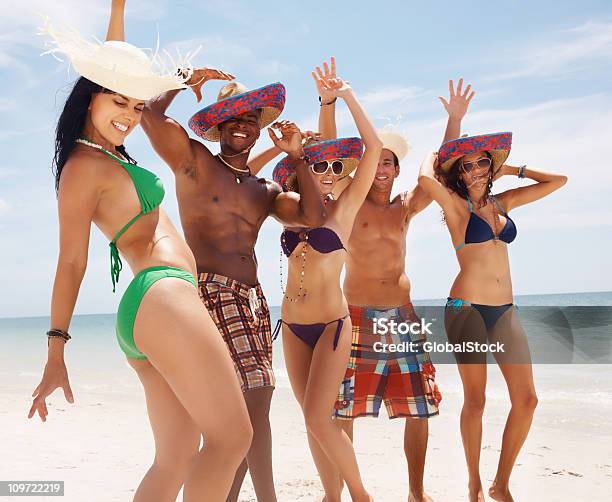 Grupo De Amigos Vestindo Sunhat Enquanto Dançar Na Praia - Fotografias de stock e mais imagens de 20-29 Anos