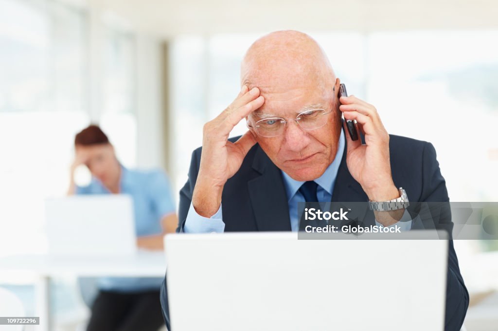 Homem de negócios com o celular enquanto estiver trabalhando em um laptop - Foto de stock de Atormentado royalty-free