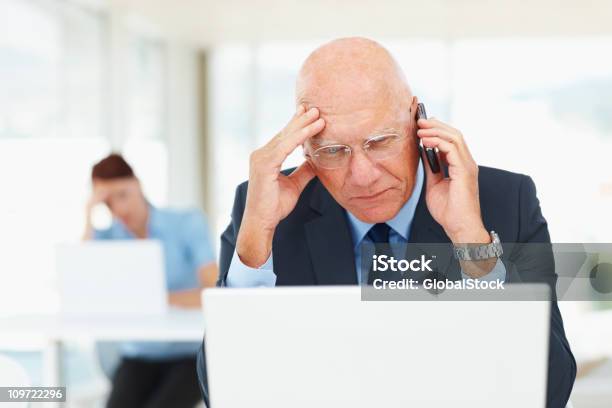 Foto de Homem De Negócios Com O Celular Enquanto Estiver Trabalhando Em Um Laptop e mais fotos de stock de Atormentado