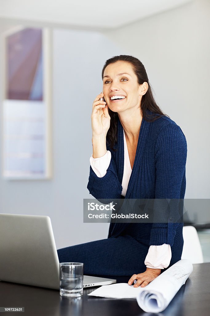 Szczęśliwa średnim wieku kobieta z komórkowy podczas pracy na laptopie - Zbiór zdjęć royalty-free (Architekt)