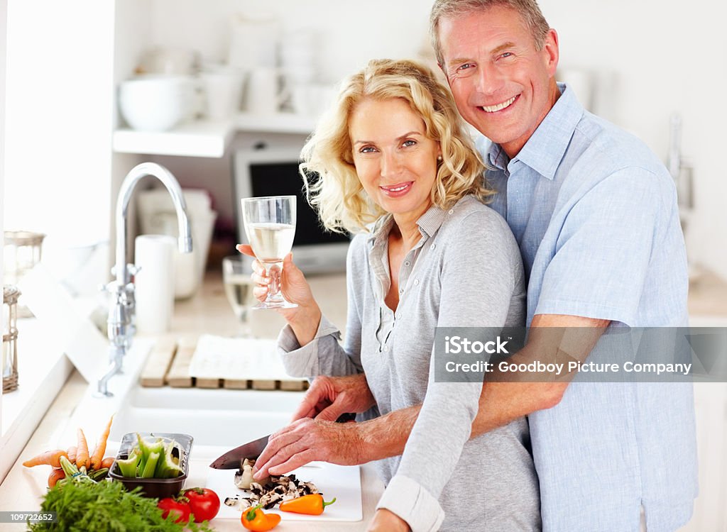 Sorridente Coppia matura sorseggiare un drink durante la preparazione di alimenti - Foto stock royalty-free di Bottiglia di vino