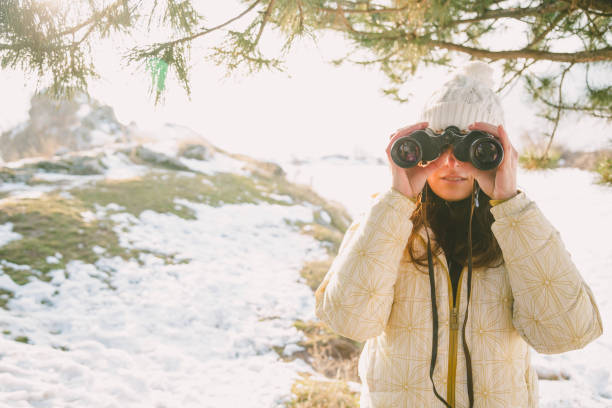 istock The girl in a White cap with a backpack in the winter in a forest looking through binoculars 1097227834