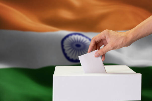 Close-up of human hand casting and inserting a vote and choosing and making a decision what he wants in polling box with India flag blended in background. stock photo