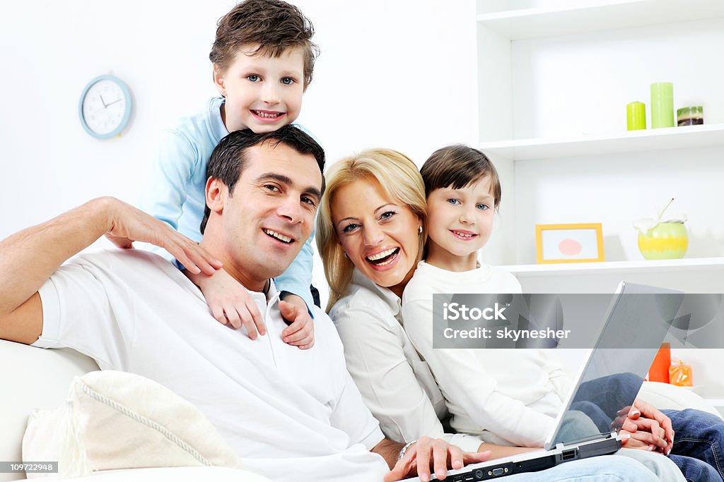 Família feliz de quatro pessoas sentado com laptop - Foto de stock de Abraçar royalty-free
