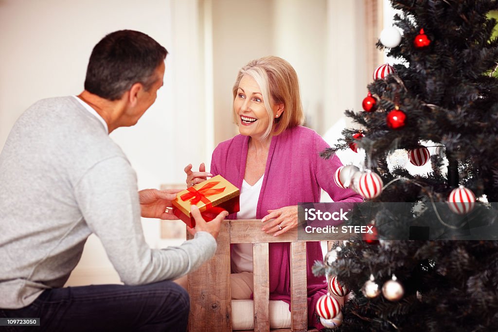 Uomo maturo dando un regalo di Natale per moglie a casa - Foto stock royalty-free di Abbigliamento casual