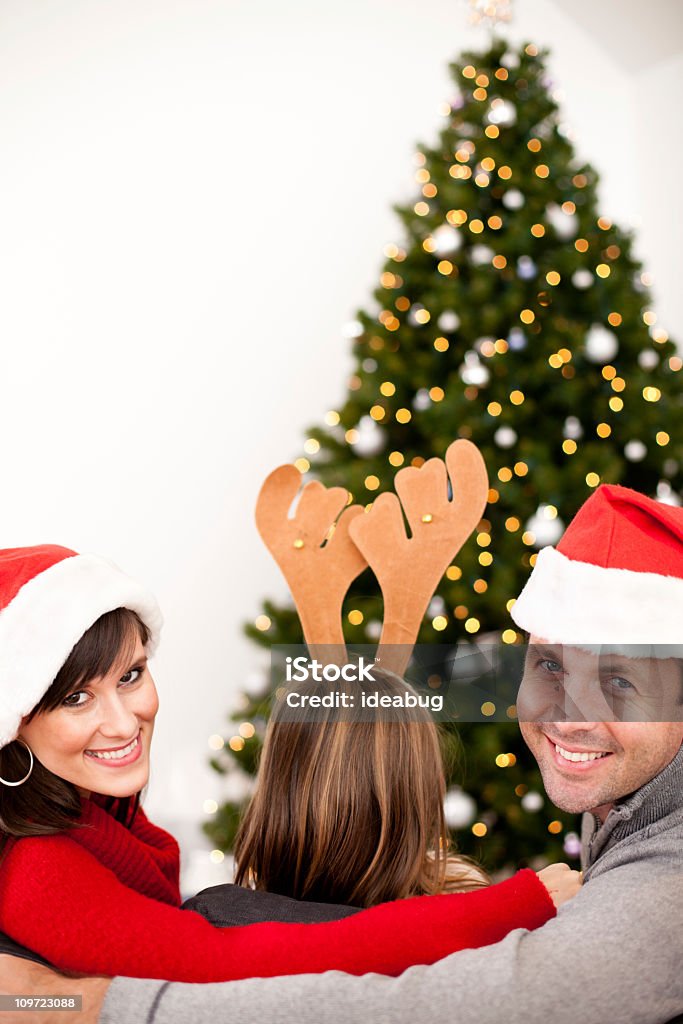 Happy Family Wearing Santa sombrero y Antlers por árbol de navidad - Foto de stock de Abrazar libre de derechos