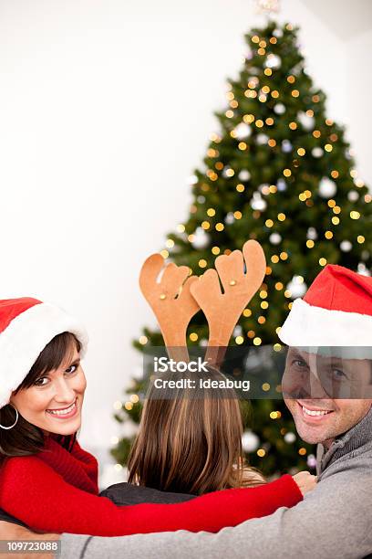 Happy Family Wearing Santa Sombrero Y Antlers Por Árbol De Navidad Foto de stock y más banco de imágenes de Abrazar