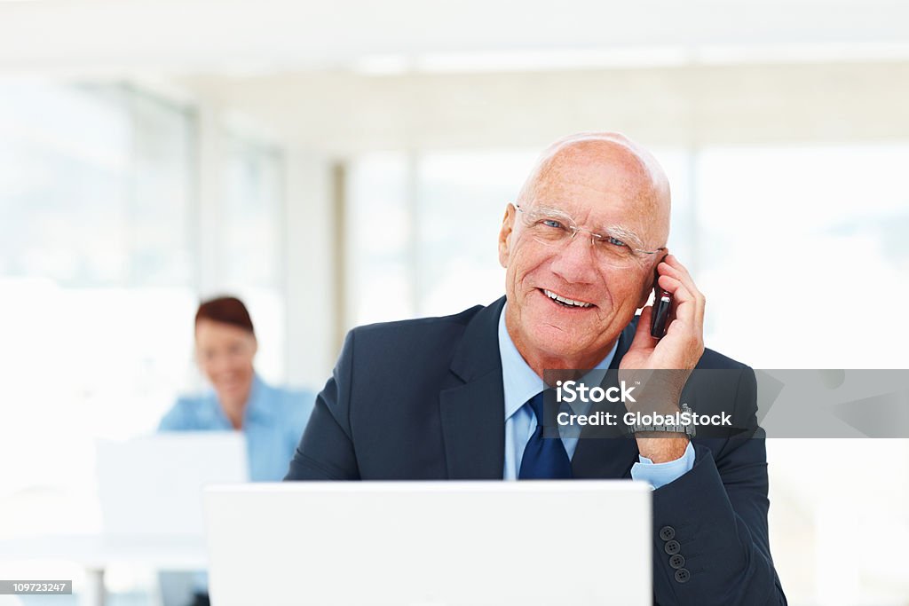 Homem idoso no cellphone enquanto trabalha em um computador portátil - Royalty-free 50 Anos Foto de stock