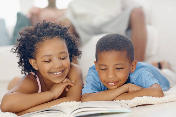 enfants lisant livre avec les parents en arrière-plan - family reading african descent book photos et images de collection