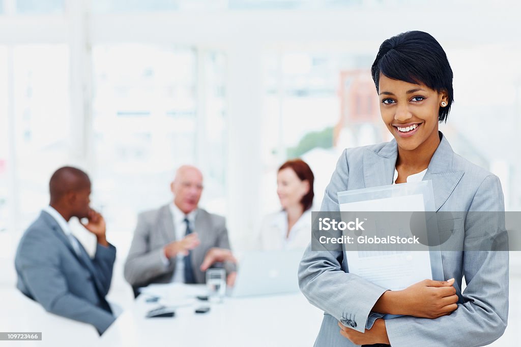 Mujer de negocios joven sosteniendo una carpeta y a su equipo en fondo - Foto de stock de Adulto libre de derechos