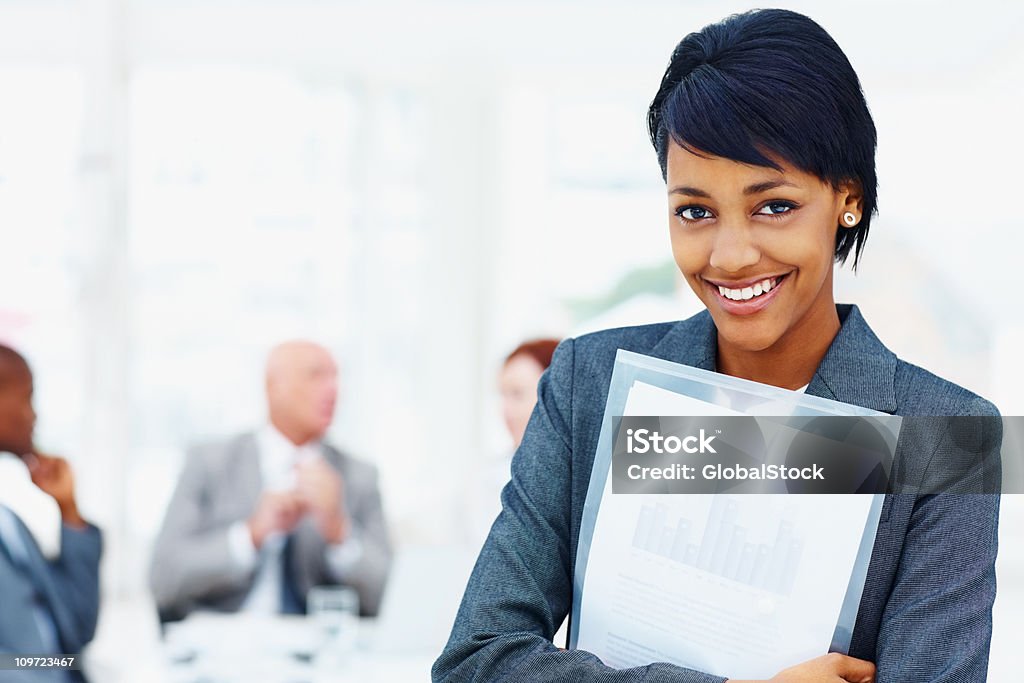 Young business female holding folder with her team in background  Adult Stock Photo