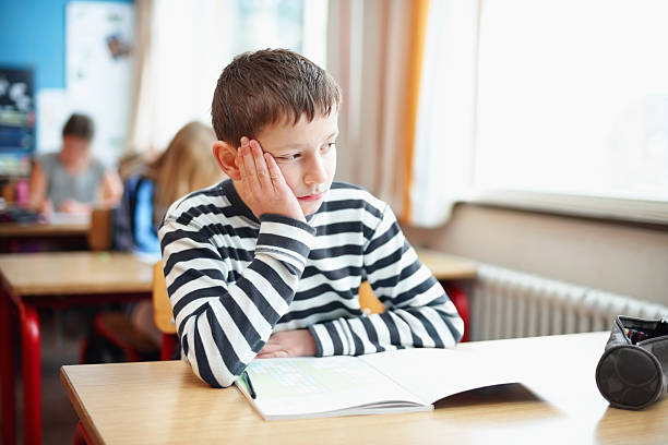 gelangweilt kleine schule junge im klassenzimmer mit blick aus dem fenster - abgelenkt stock-fotos und bilder