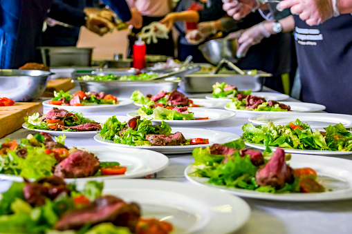 Cooked Roast Beef, Fresh Salad And Tomatoes Served On White Plates. Cooking Master Class, Workshop with People Learning How to Cook Around the Table